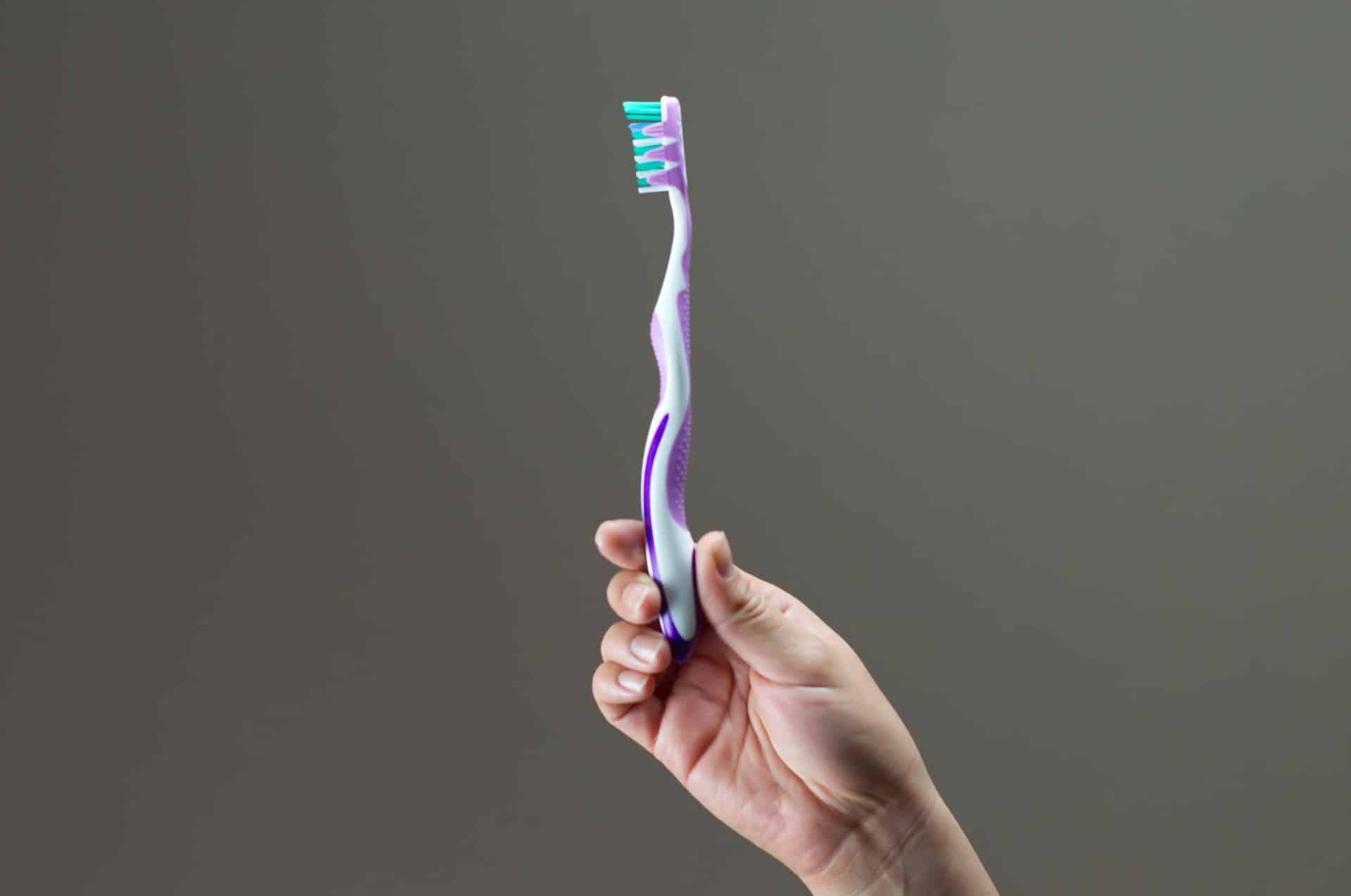 brushing teeth too hard - hand holding a toothbrush upright