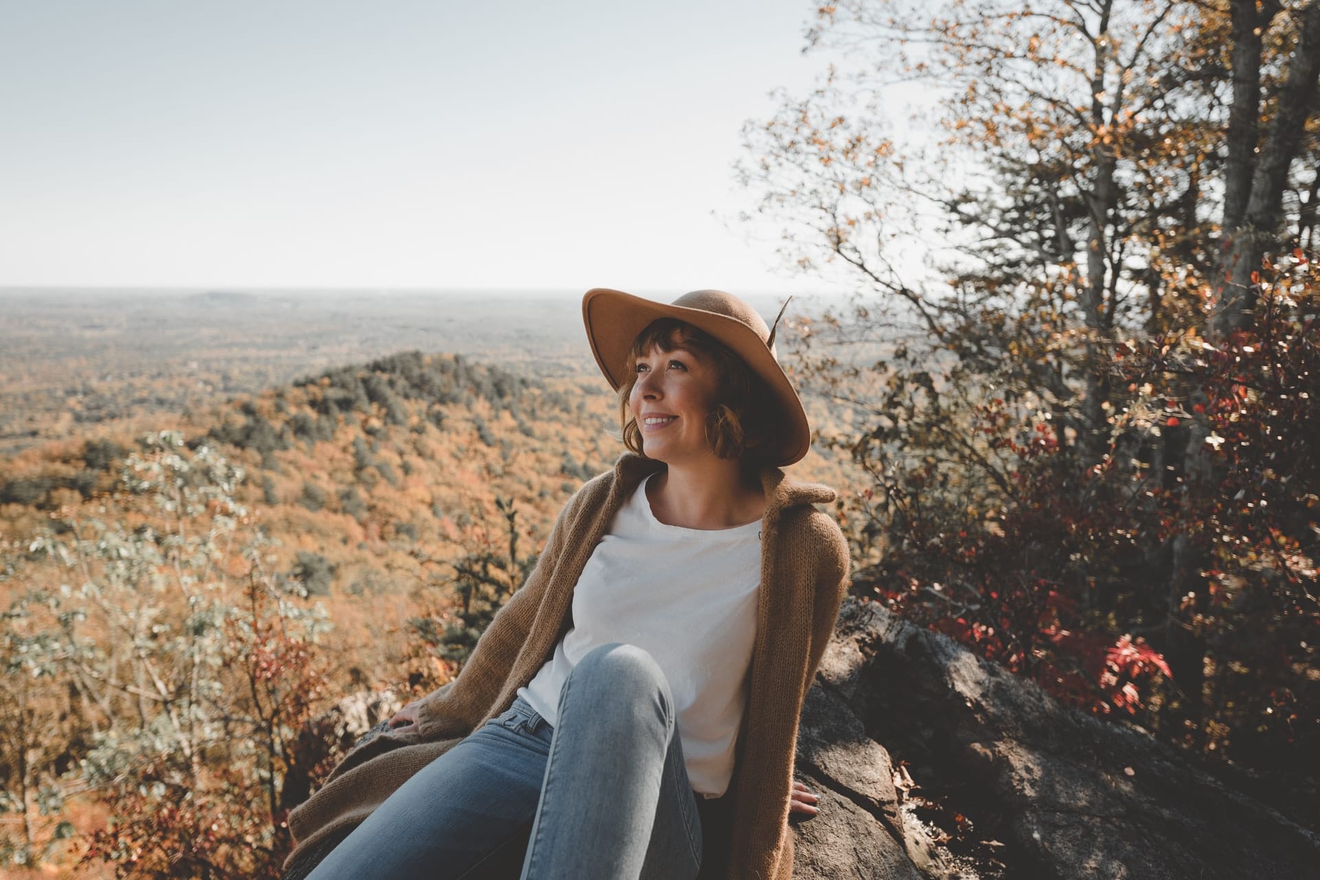 woman in hat smiling on rock with mountain behind