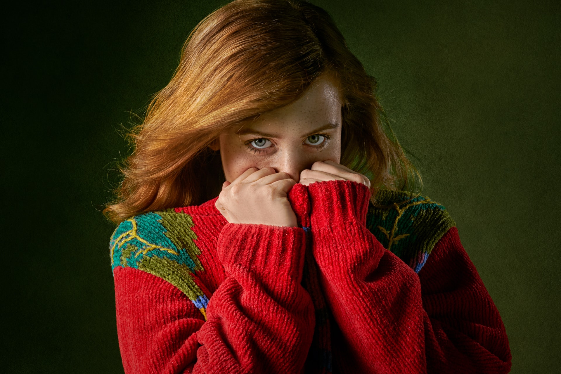 girl in red sweater looking nervous with green background