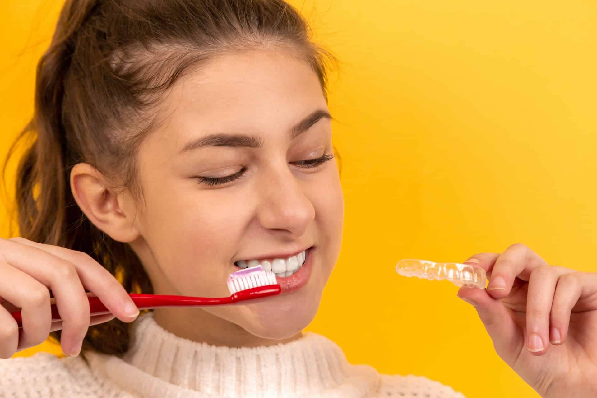 how to clean invisalign - woman holding toothbrush and clear aligner